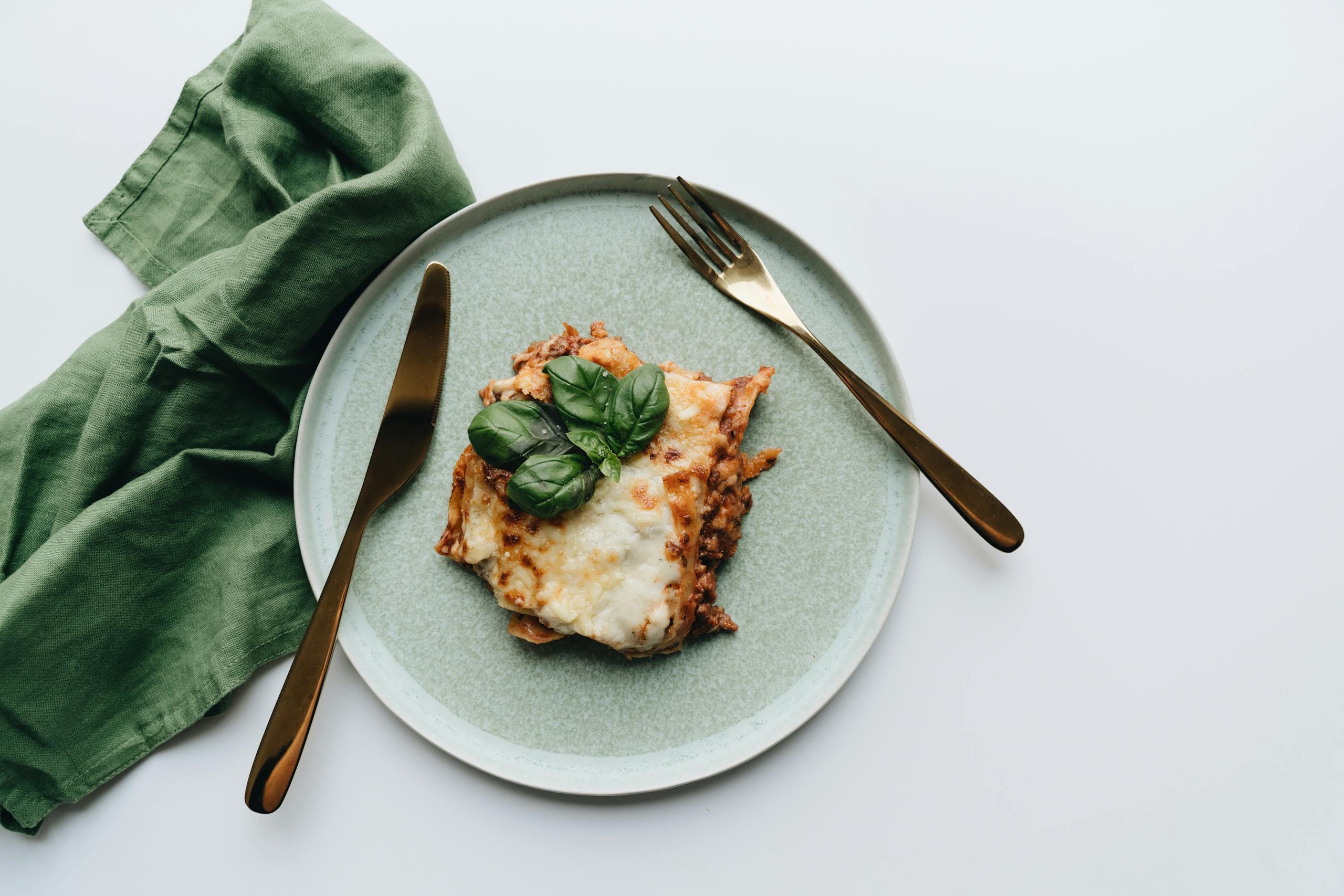 A flatlay of traditional Italian lasagna garnished with fresh basil, styled with elegant cutlery.