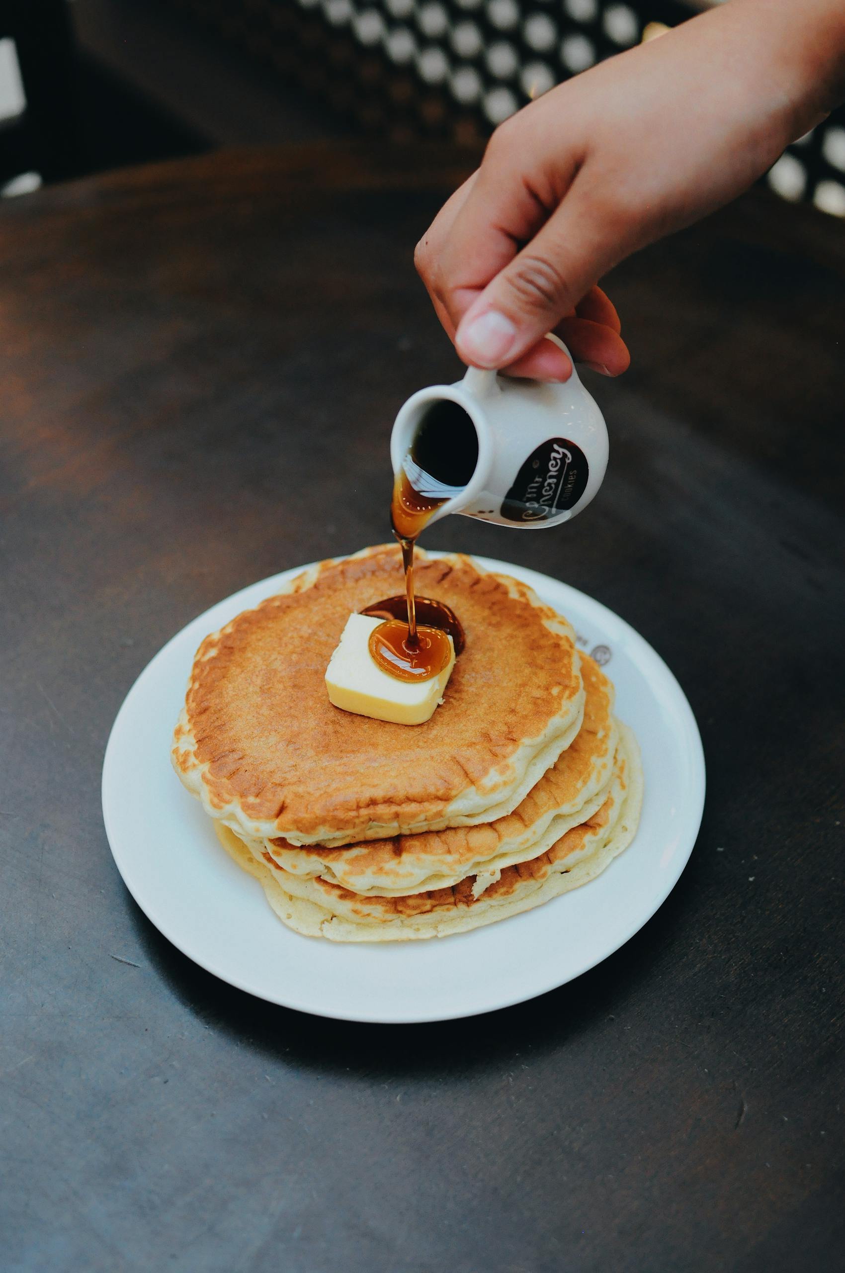 Delicious stack of pancakes topped with butter and maple syrup being poured.