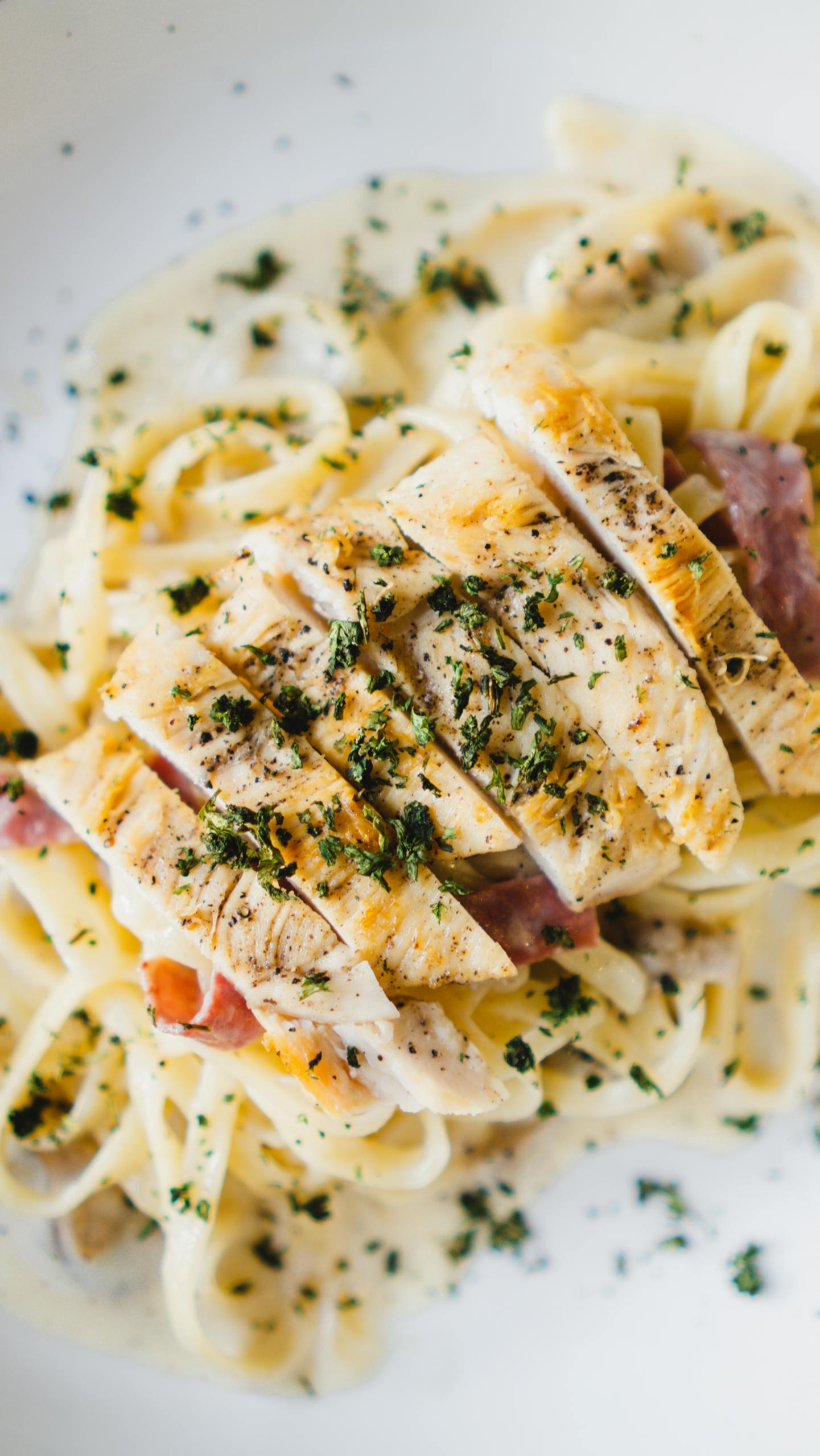 Savor a close-up of creamy chicken fettuccine pasta garnished with parsley, perfect for lunch or dinner.