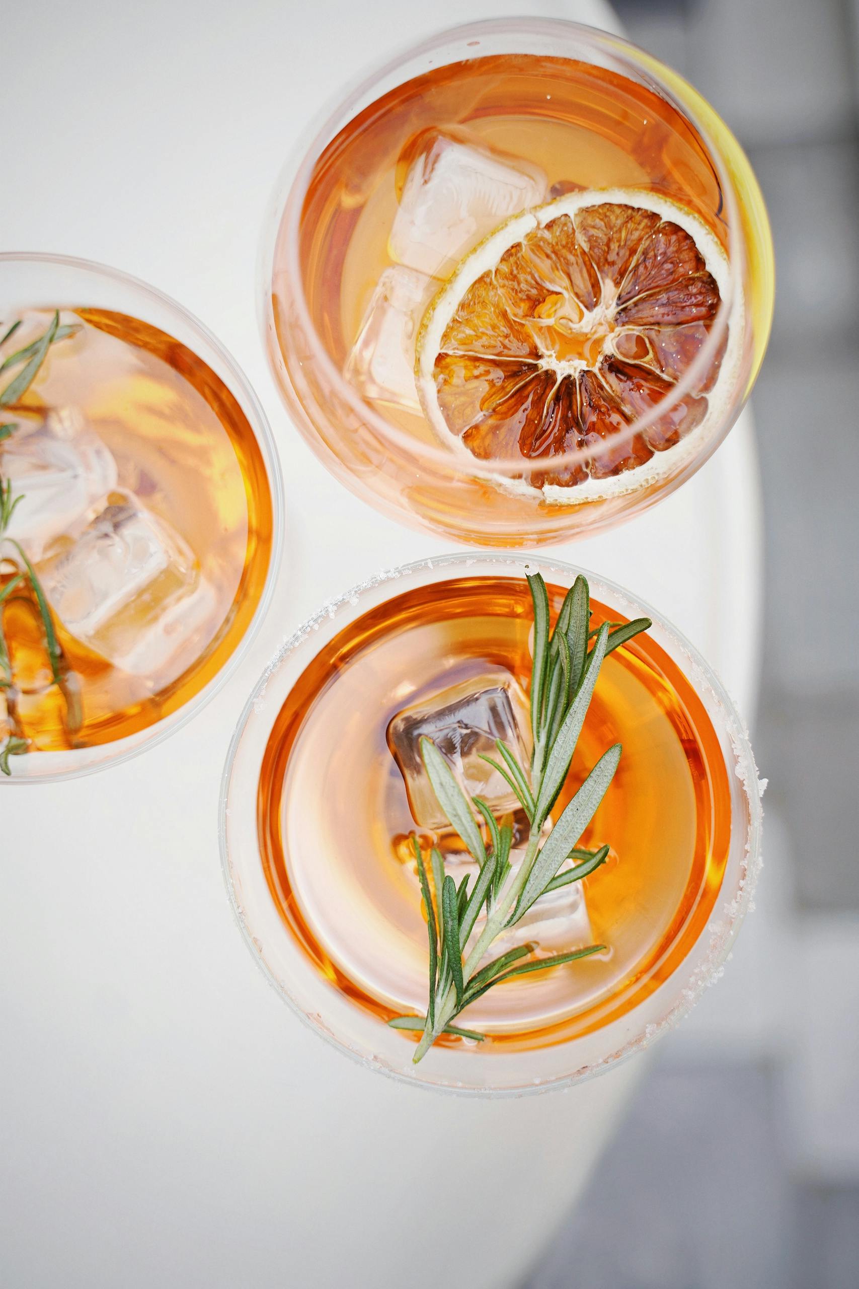 Top view of three citrus and rosemary cocktails with ice and garnish on a summer day.