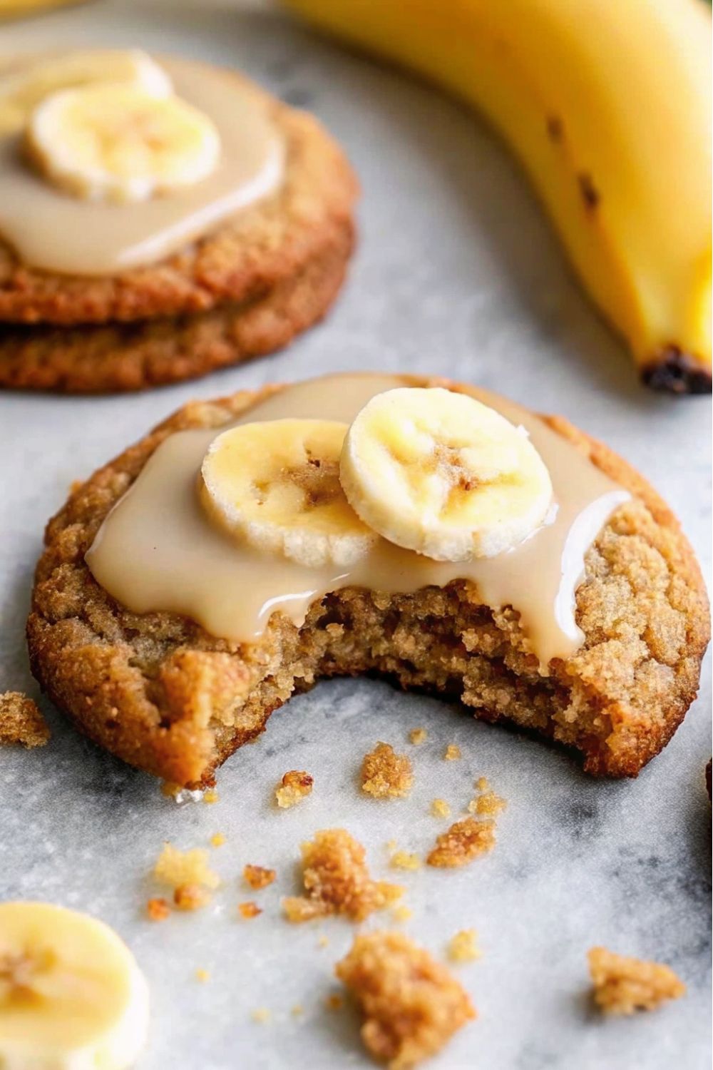 Banana bread cookies with glaze icing and banana slice on top with a bite taken.